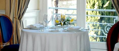 Mesa de comedor dispuesta para cuatro, con mantel blanco, platos, vasos y un centro de mesa con flores amarillas.