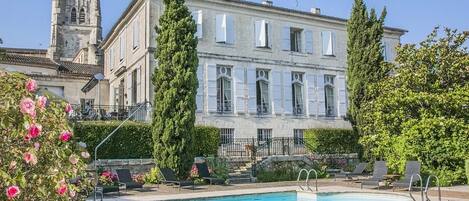 Una piscina con sillones de descanso y un edificio con una torre al fondo.