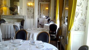 A dining area with round tables set for four, each with white tablecloths, chairs, and wine glasses.