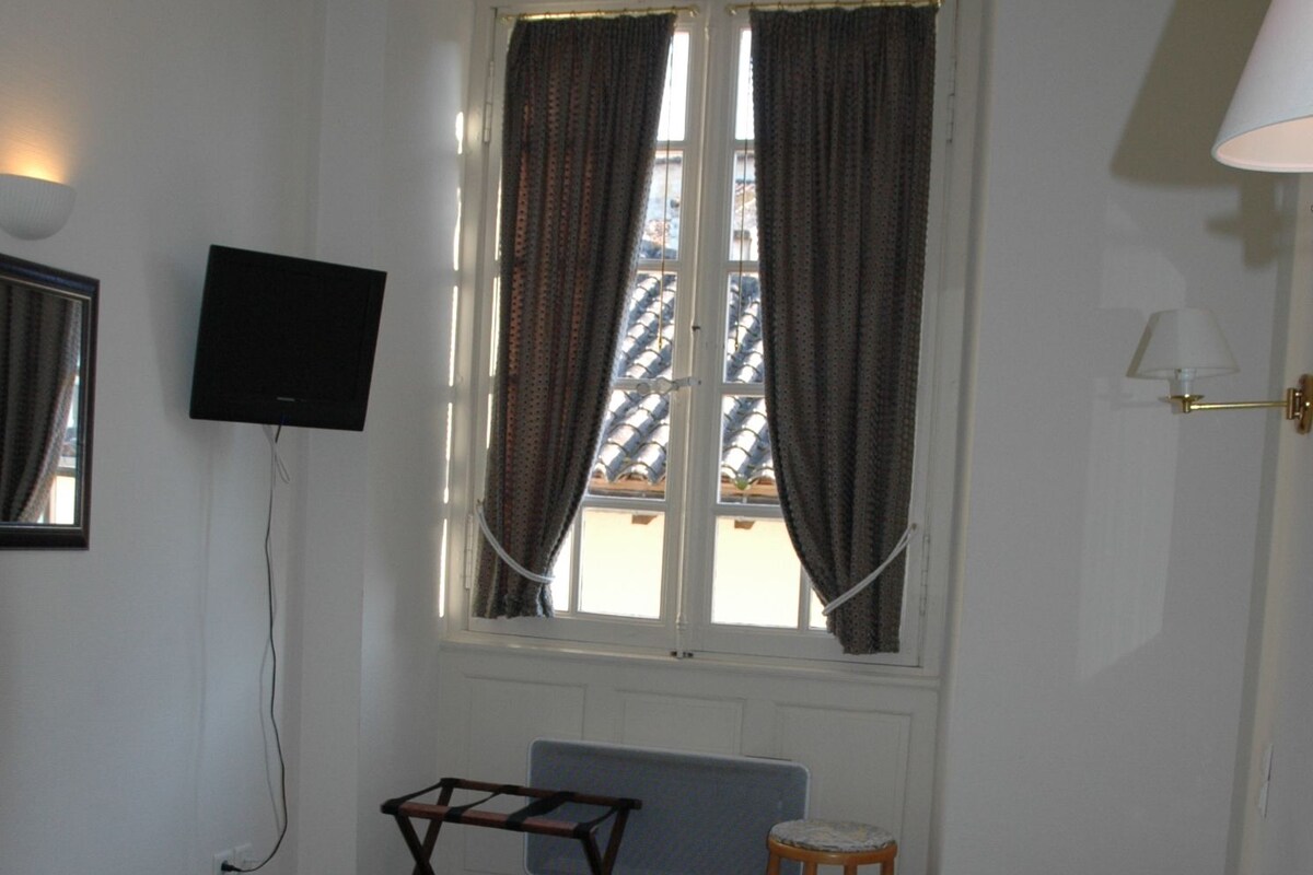 A hotel room with a bed, a desk, a chair, a TV, and a window with curtains.