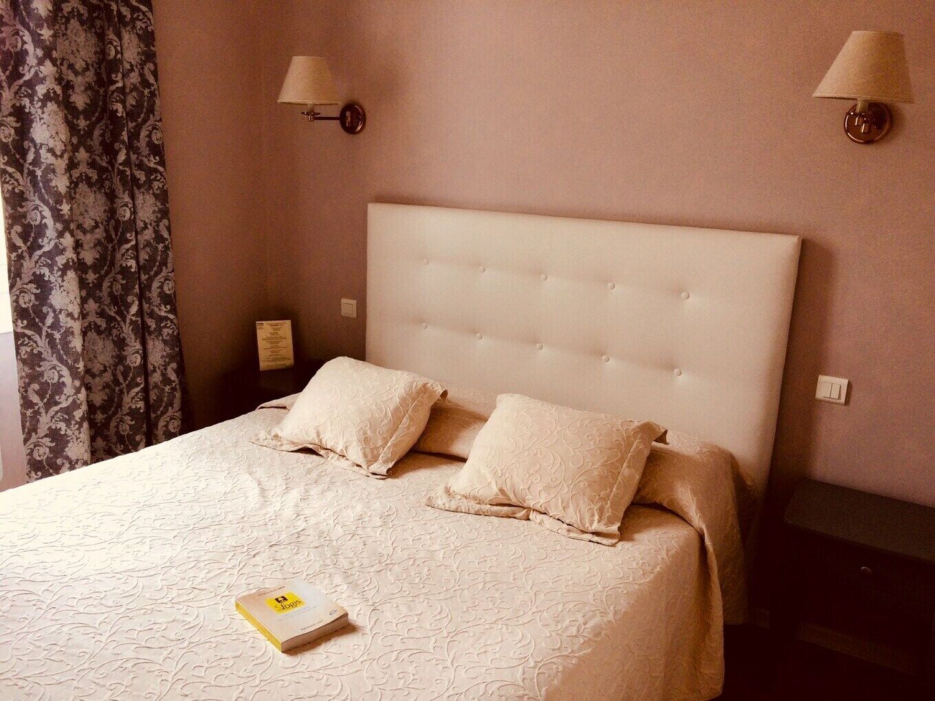 A neatly made bed with a tufted headboard, two pillows, and a book on the bed.