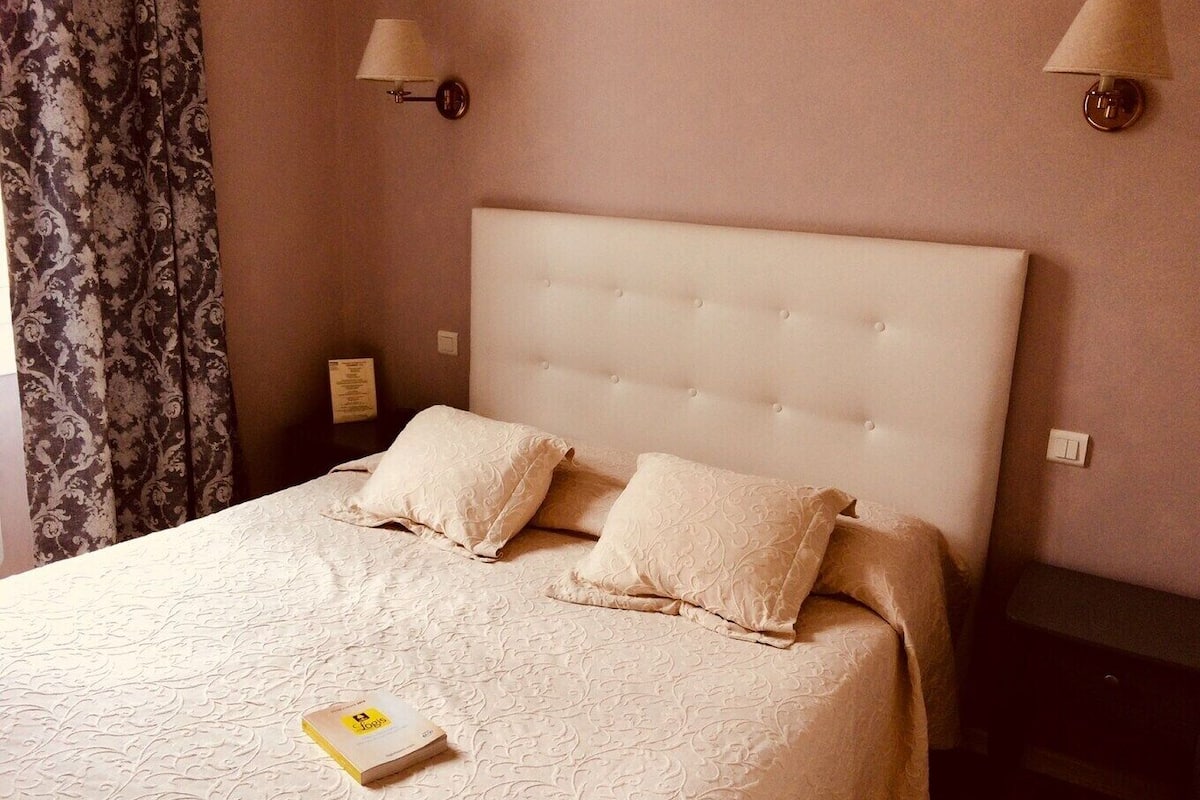A neatly made bed with a tufted headboard, two pillows, and a book on the bed.