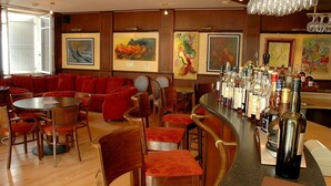 A bar area with a counter displaying various bottles, a seating area with red upholstered sofas and chairs, and artwork on the walls.