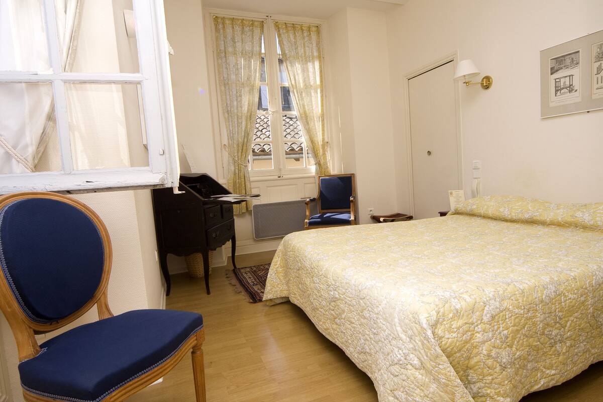 A bedroom with a bed, a desk, a chair, and a window with curtains.