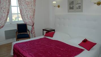 A room with a bed, a chair, a nightstand, a window with curtains, and wall-mounted artwork.