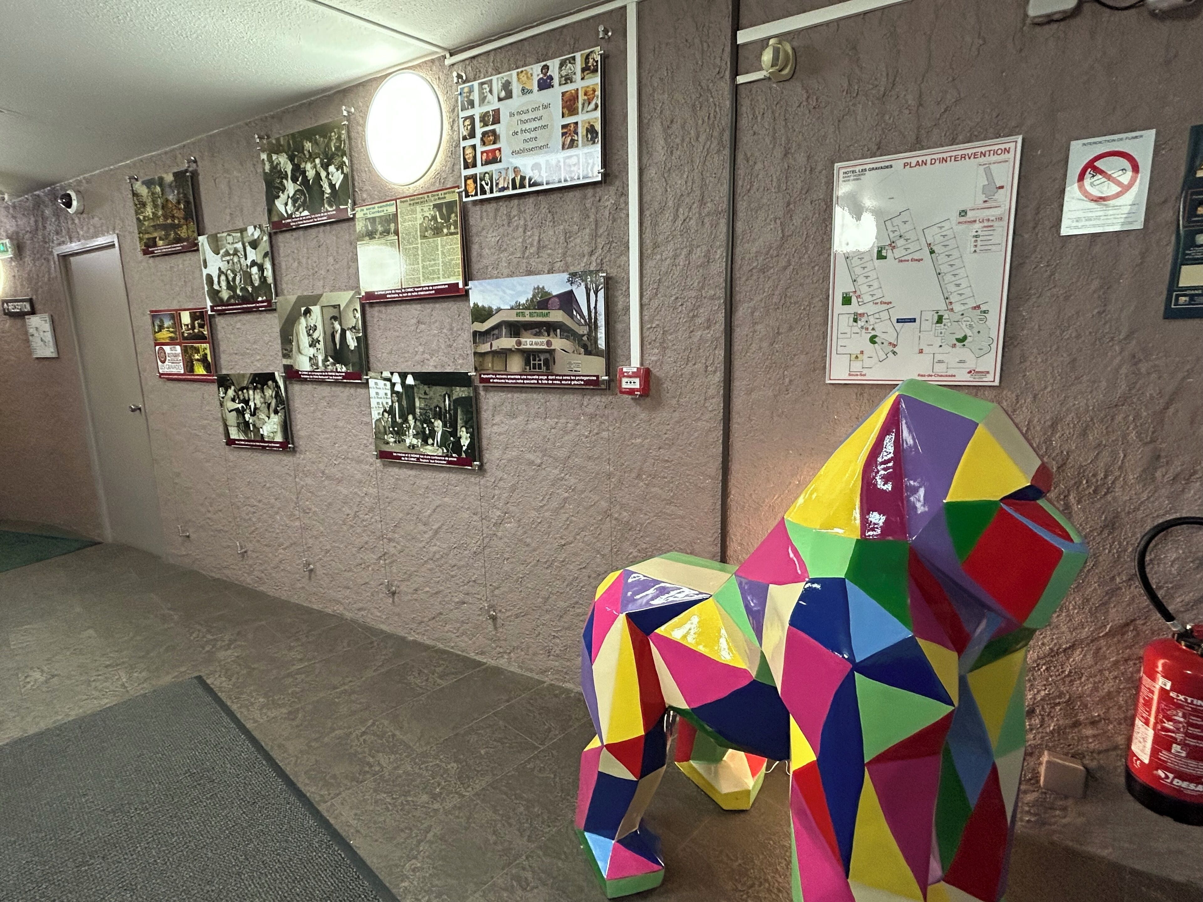 A hallway with a colorful geometric sculpture, a fire extinguisher, and various informational posters on the wall.