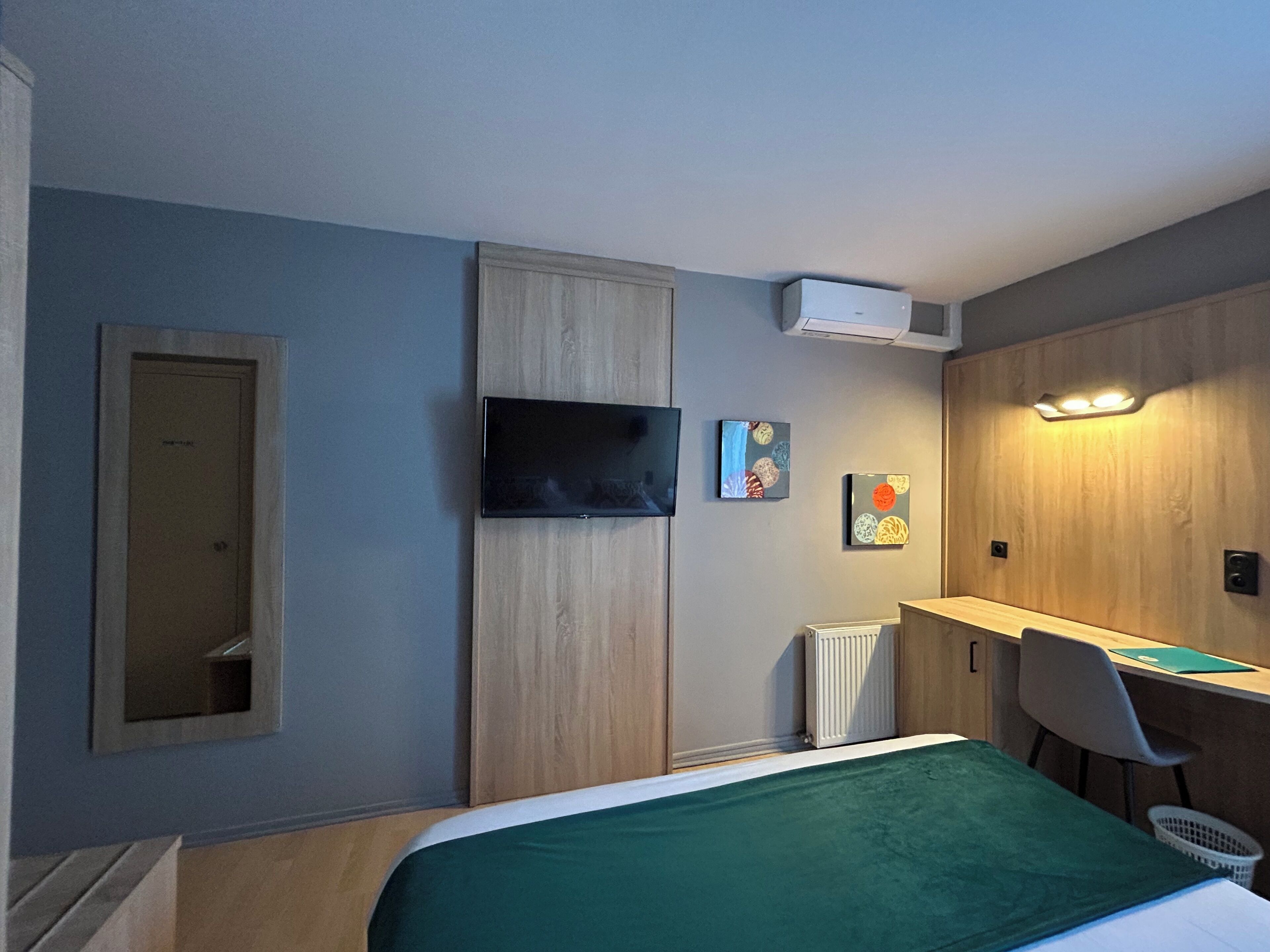 A hotel room with a bed, a desk, a chair, a television, and artwork on the walls.