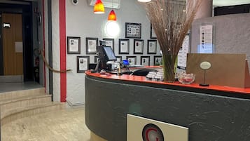 A reception desk with a modern design, a security camera, framed pictures on the wall, and a vase with dried plants.