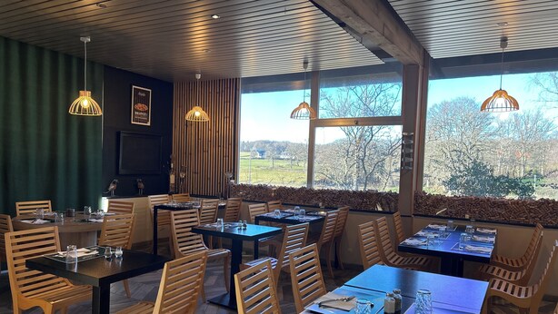 A restaurant with wooden furniture, large windows, and a view of the countryside. - Hotel Les Gravades (Ussel)