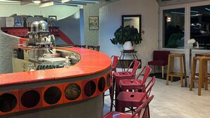 A bar area with a circular counter, red bar stools, and a potted plant. - Hotel Les Gravades (Ussel)