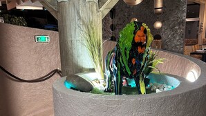 A circular water feature with a stone base, surrounded by a textured wall and a wooden bench. - Hotel Les Gravades (Ussel)