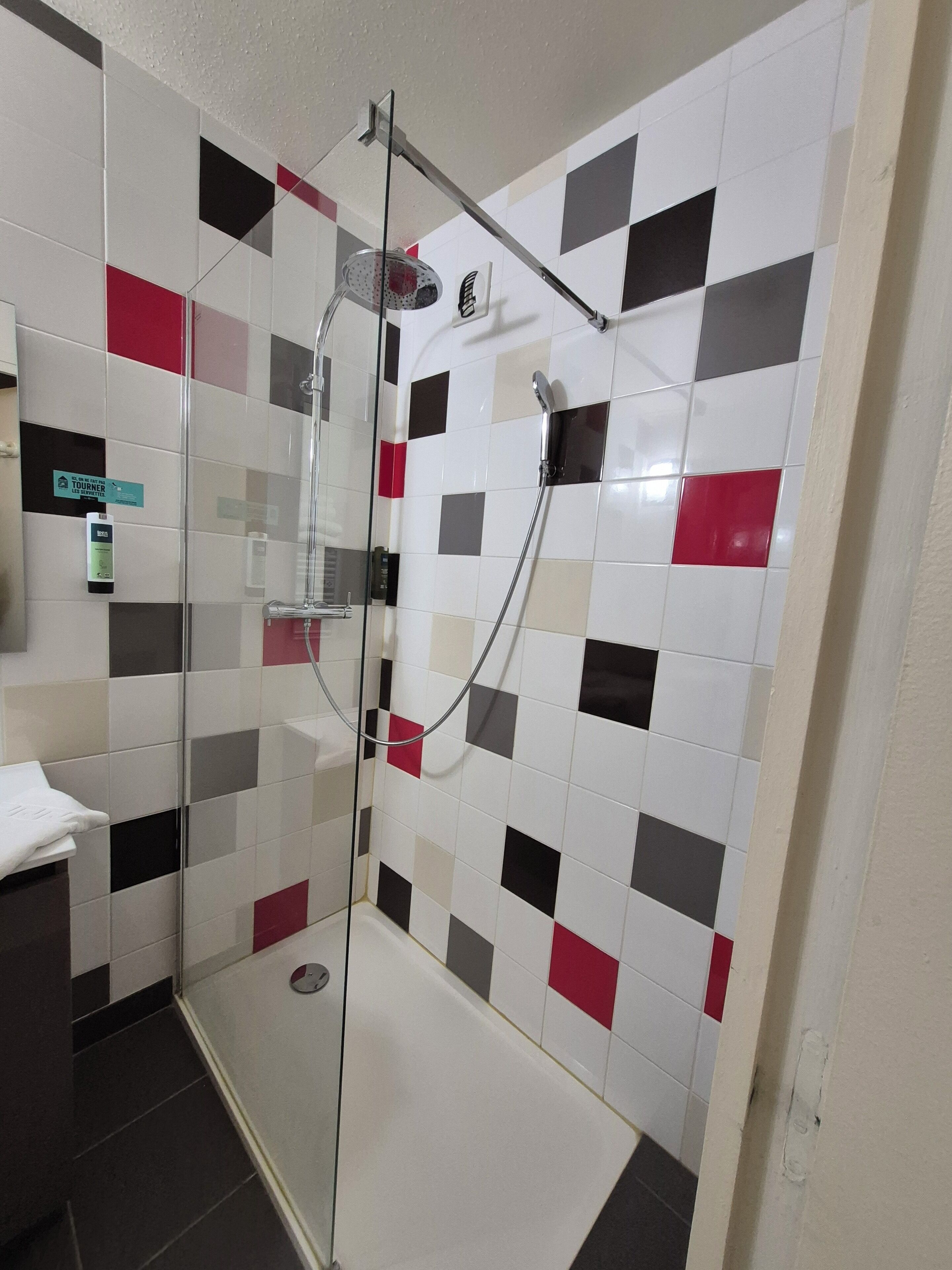A shower area with a glass door, a handheld showerhead, and a wall-mounted faucet.