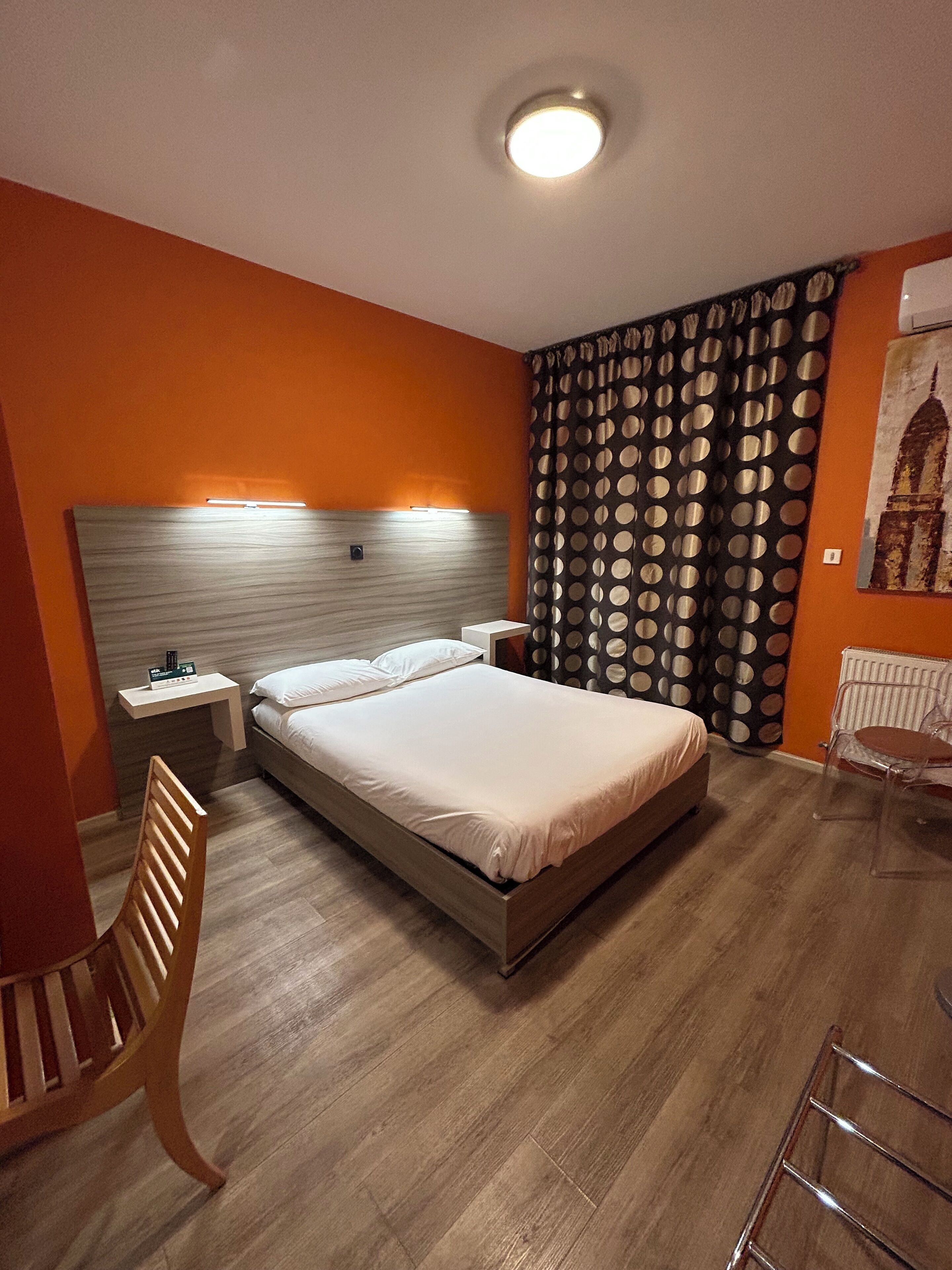 Habitación de hotel con cama, suelo de madera, una mesita de noche, una silla y una cortina de lunares.