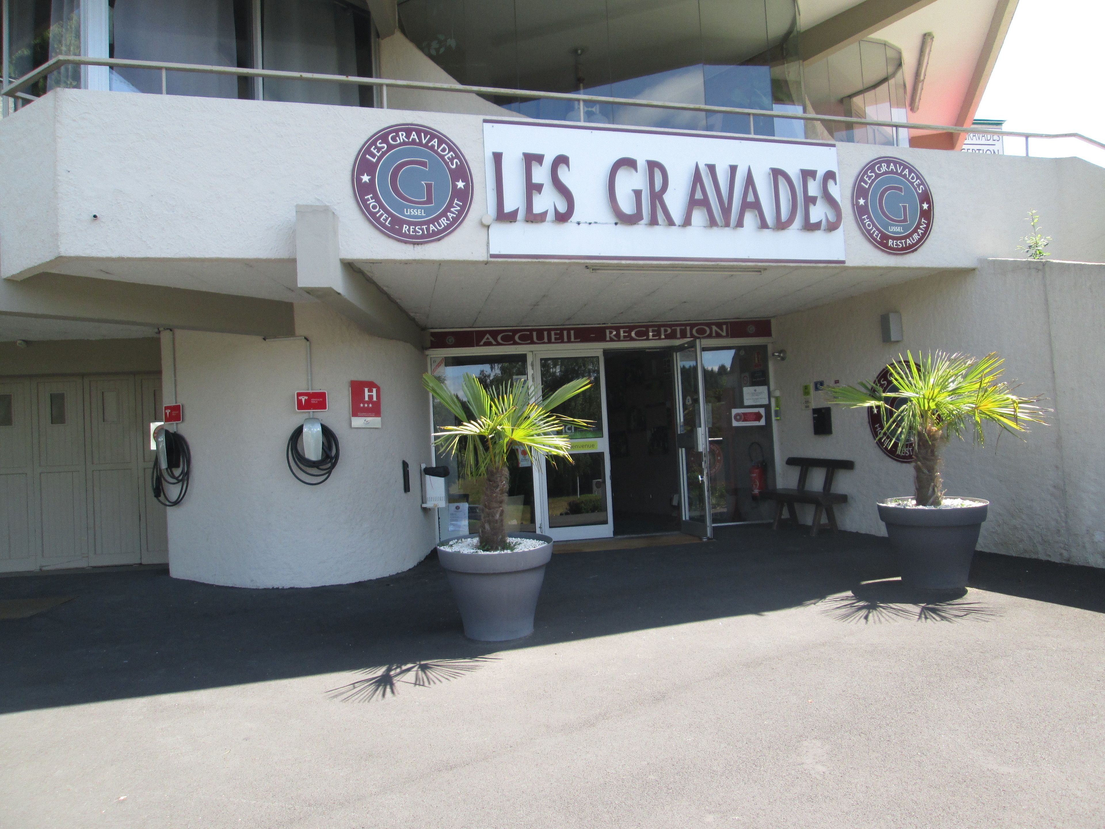 The exterior of Les Gravas Hotel with a reception area, two potted plants, and a parking sign.