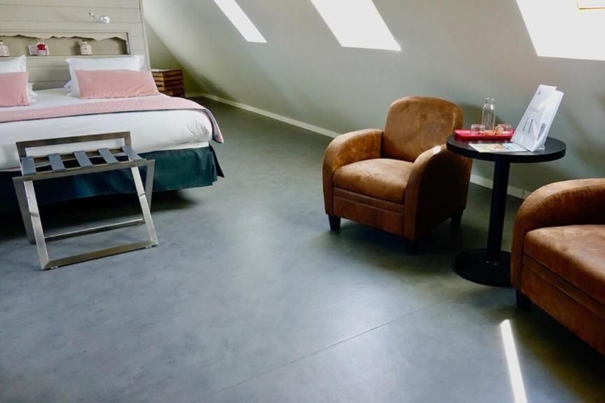 A bedroom with a bed, two armchairs, a small table, and a ladder.