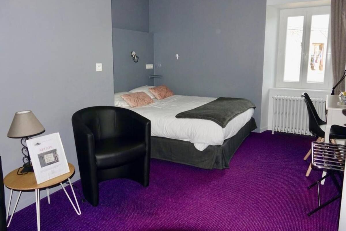 A hotel room with a bed, a chair, a desk, and a window.
