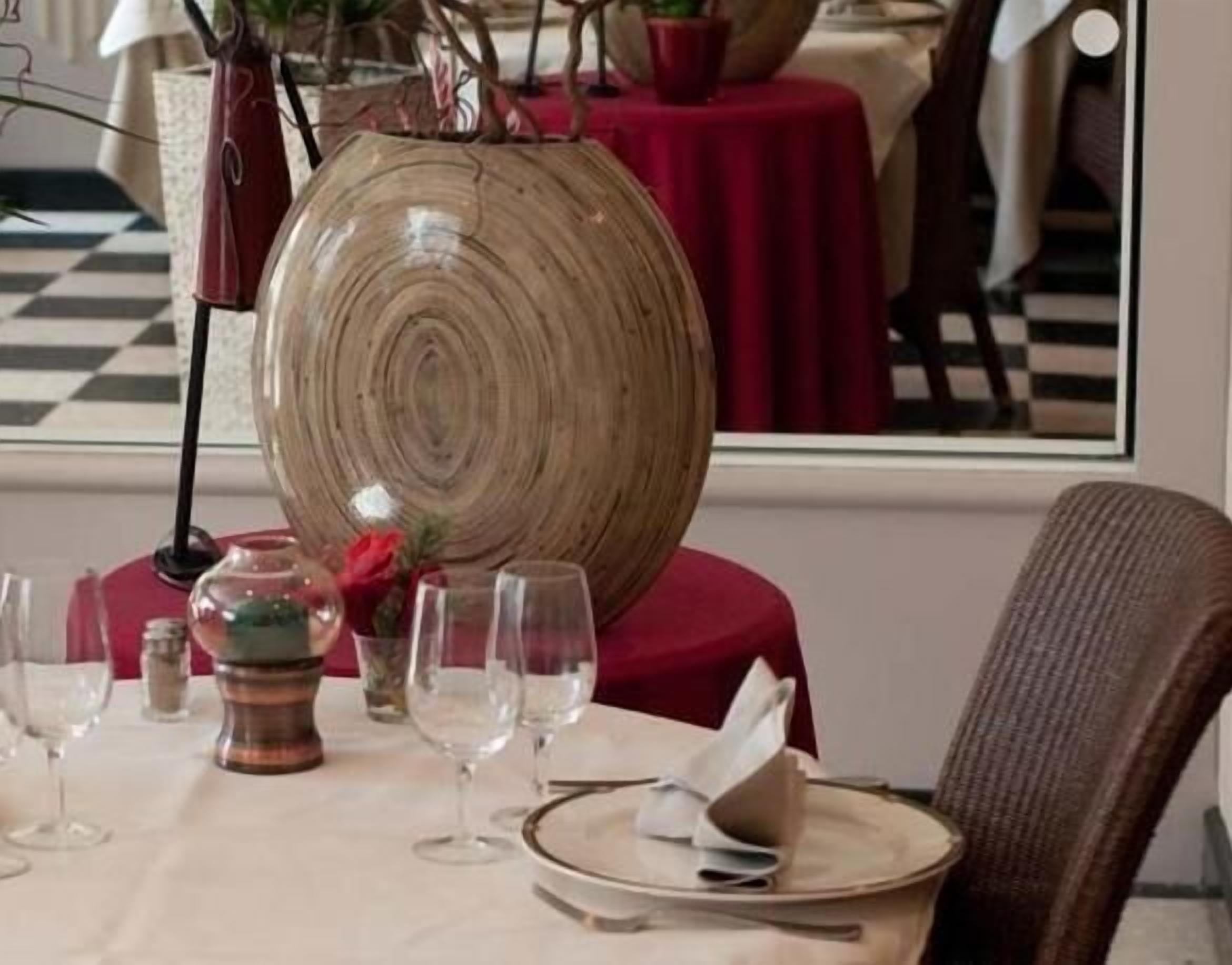 Una mesa de comedor con un cuenco de madera grande como centro de mesa, copas de vino transparentes y un mantel rojo.