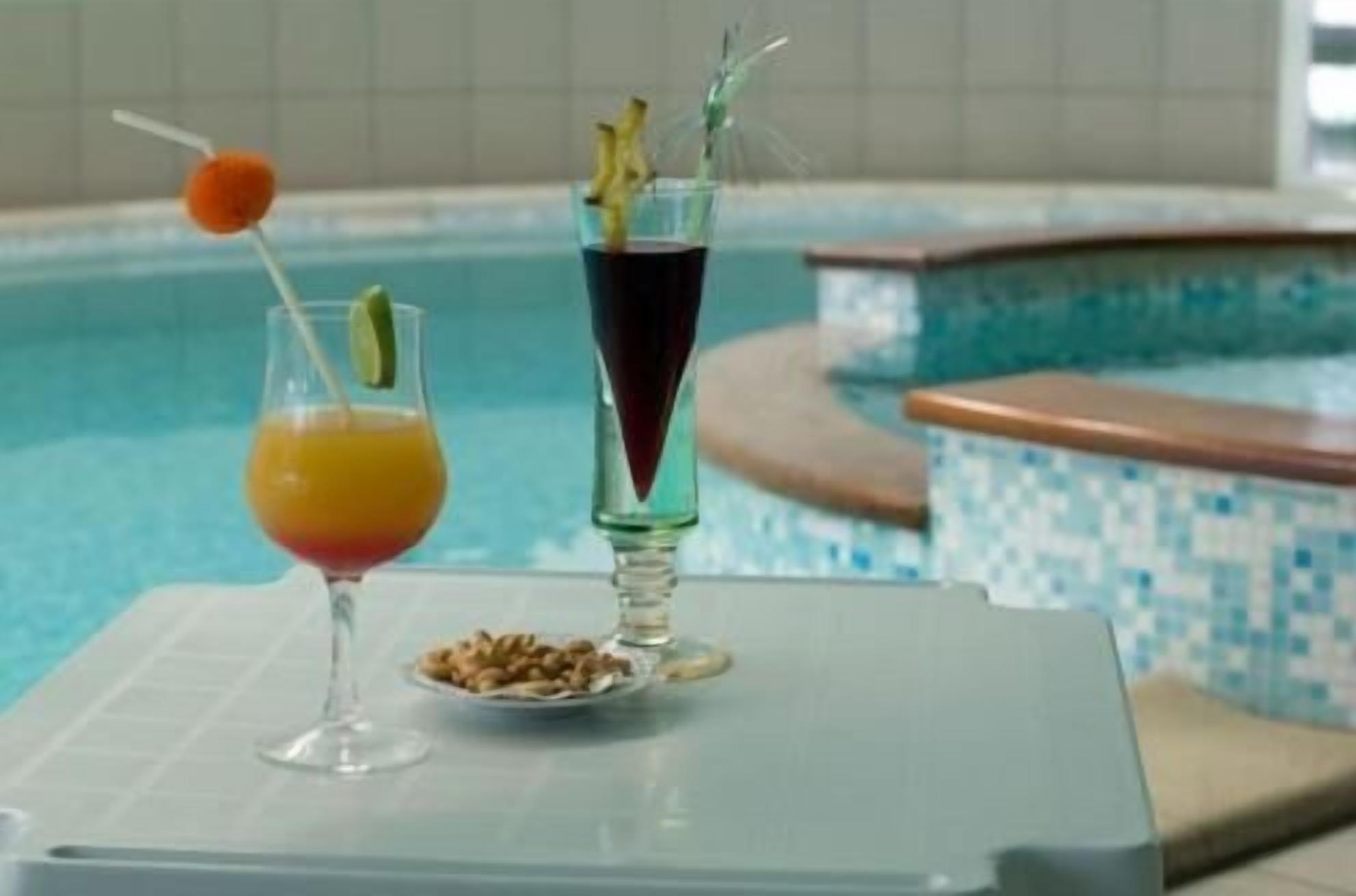 A poolside setting with two drinks, one in a glass and one in a tall glass with a straw.