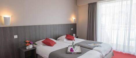 A hotel room with two beds, a red carpet, and a large window with curtains.
