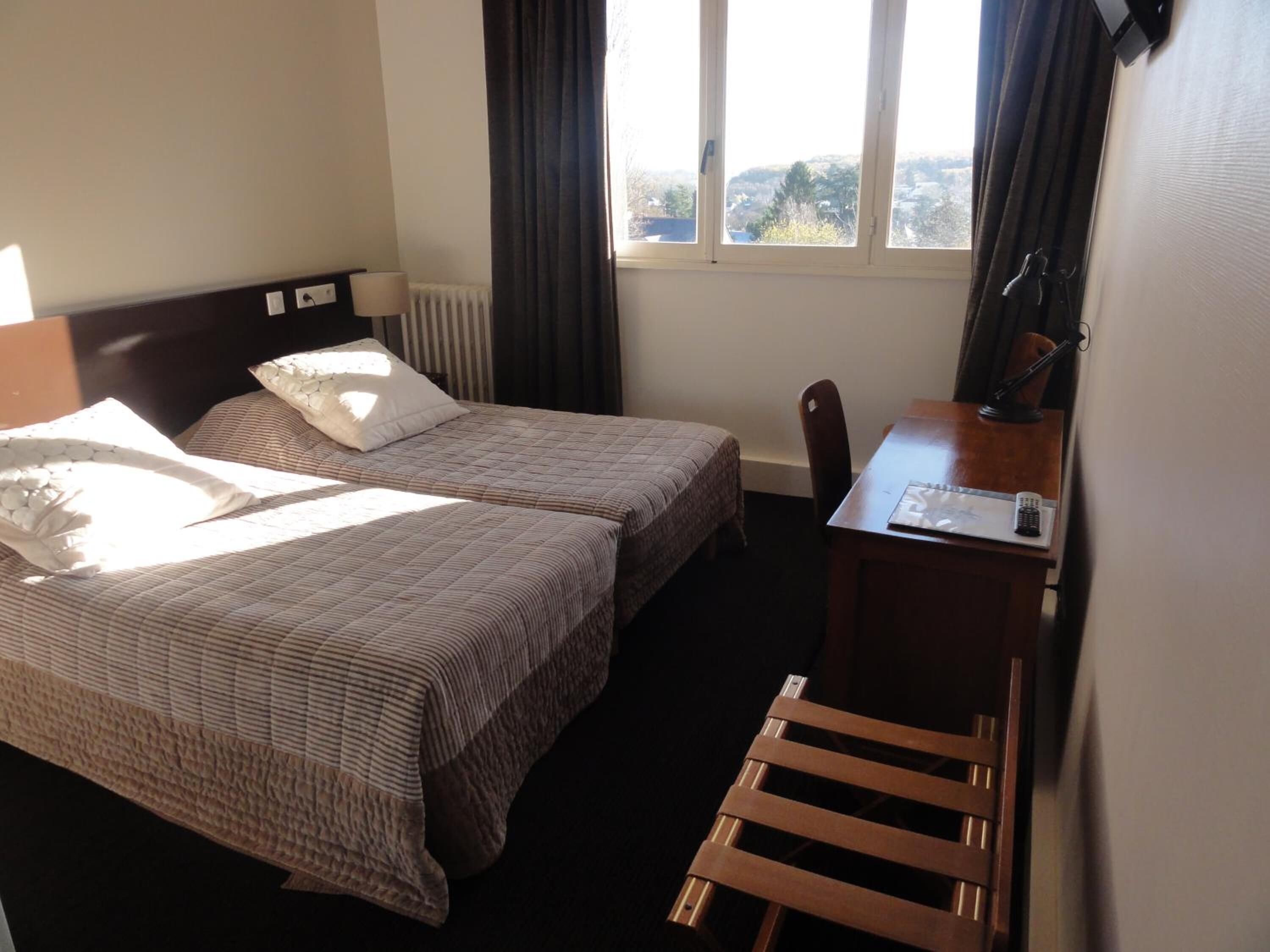A hotel room with two beds, a desk, a chair, and a window with a view of the outdoors.