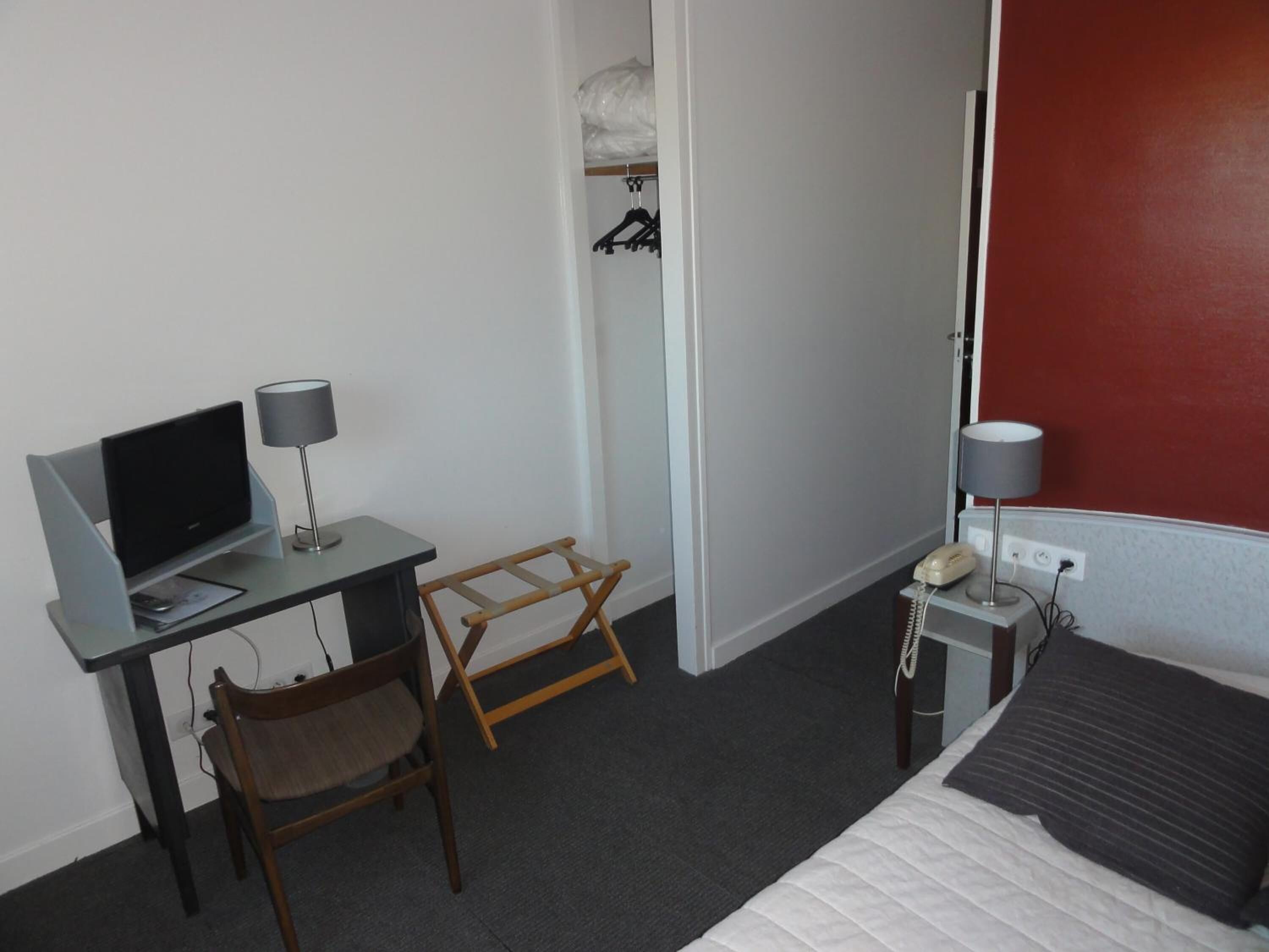 A hotel room with a bed, a desk with a computer and lamp, a chair, a telephone, and a wardrobe.