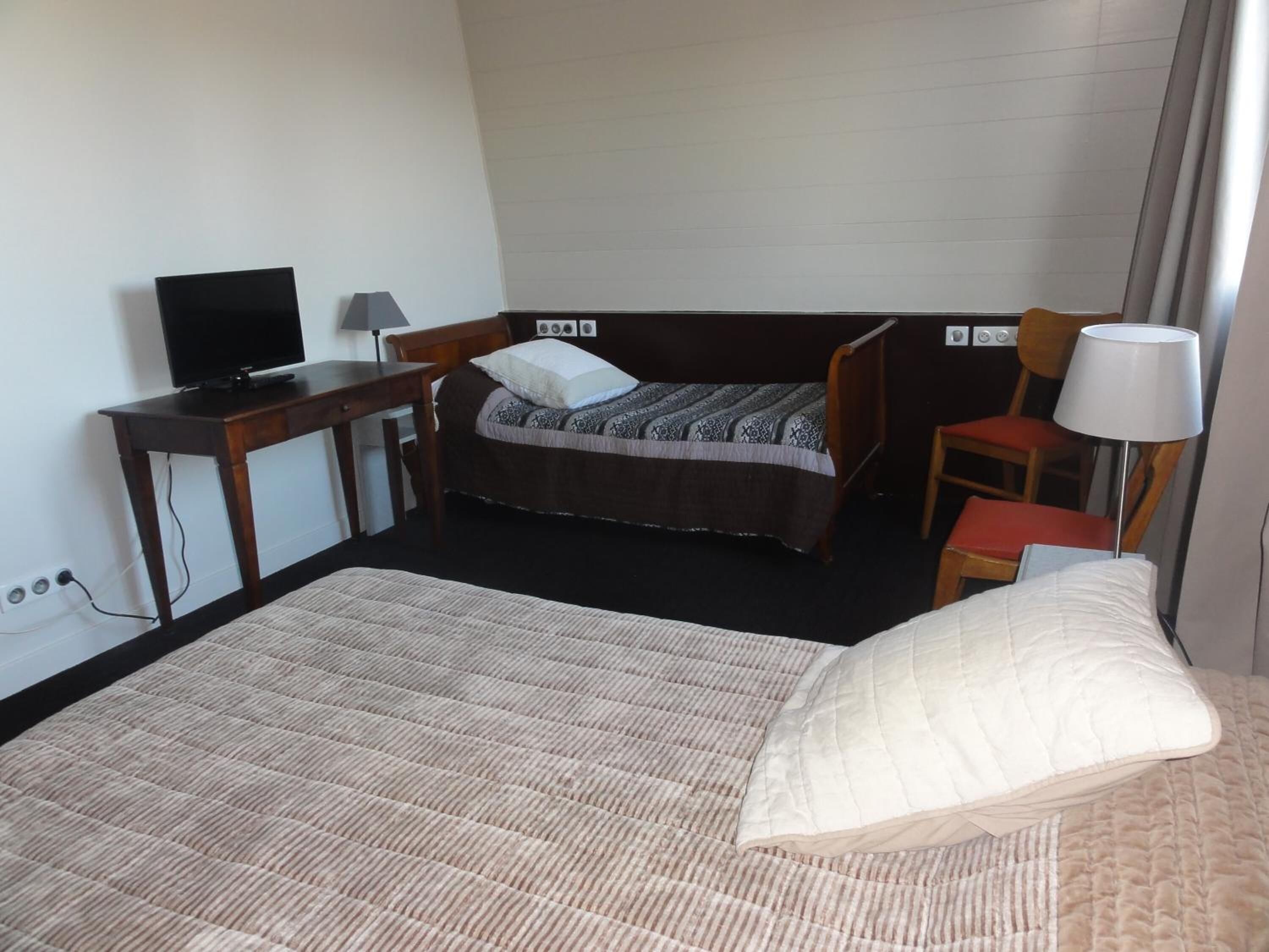 Una habitación de hotel con una cama, un escritorio, una silla, un televisor y una lámpara.