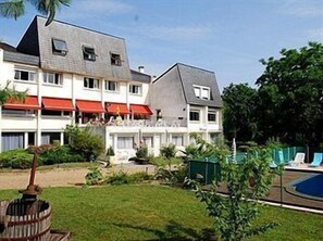 Ett hotell med flera våningar, en swimmingpool och en välskött trädgård.