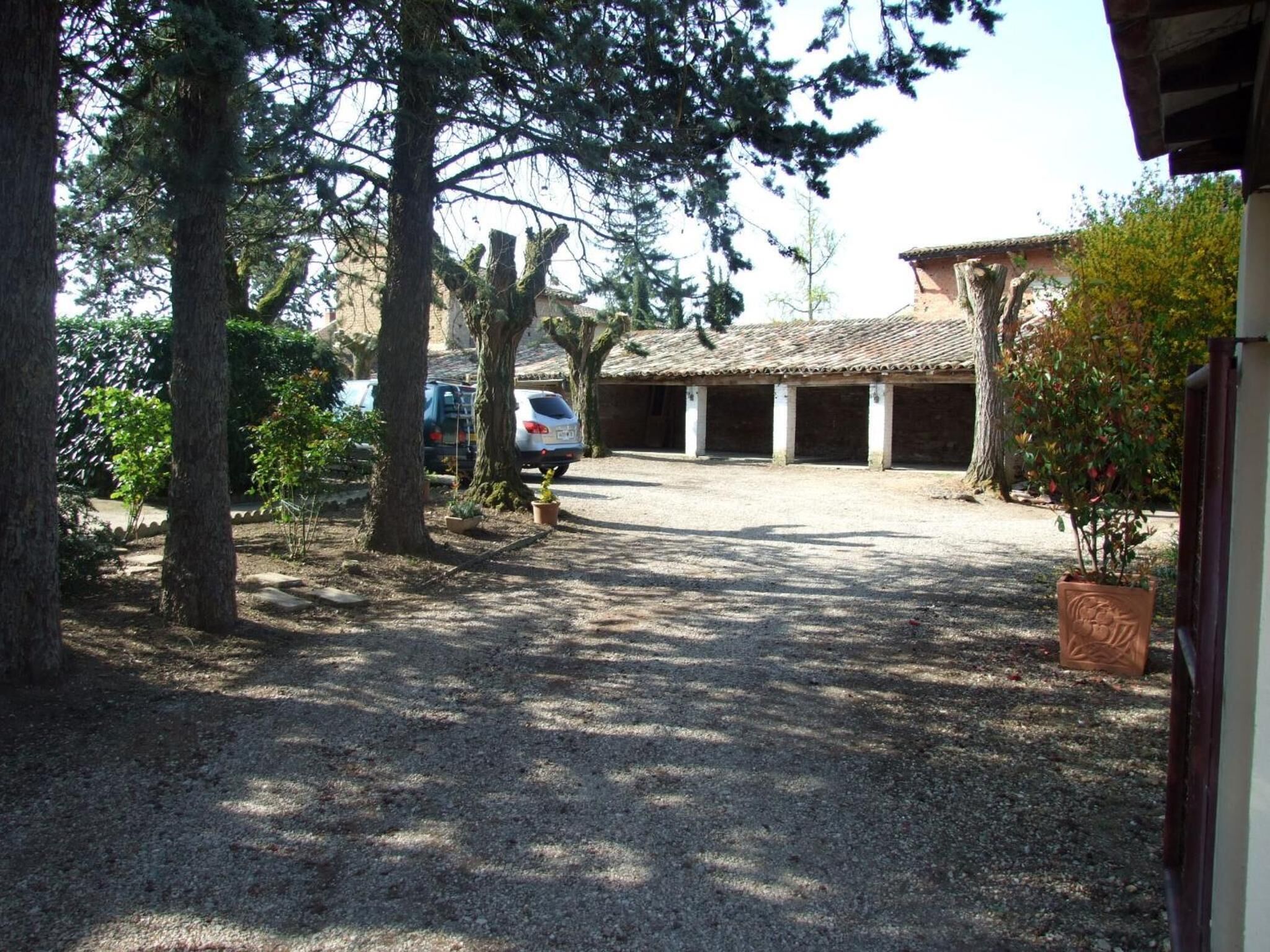 A gravel driveway leading to a building with a tiled roof and columns. There are trees and a parked car visible.