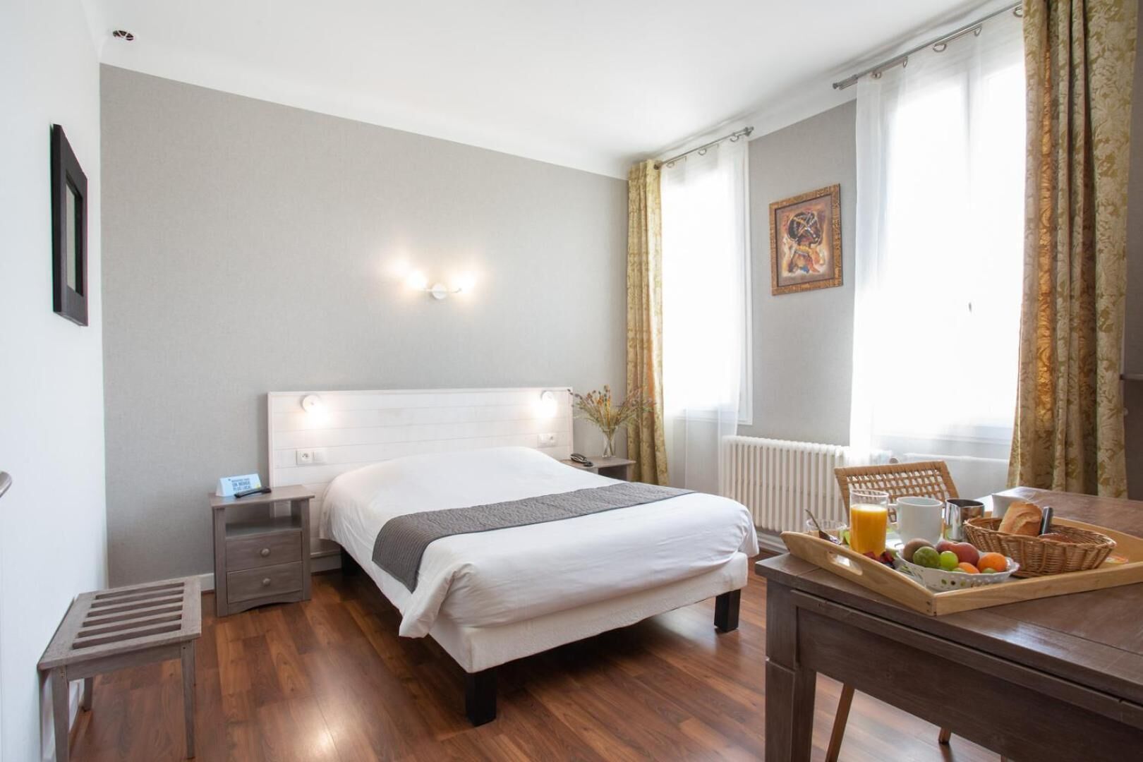 Habitación de hotel con cama, mesita de noche, y una bandeja de desayuno con frutas y jugo.