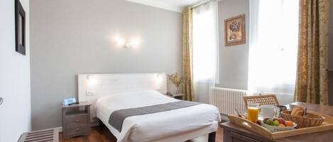 Habitación de hotel con cama, mesita de noche, y una bandeja de desayuno con frutas y jugo.