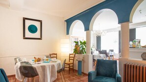 A dining area with a table set for two, a potted plant, and a view through an archway to another room. - Hôtel l'Occitan (Gaillac)