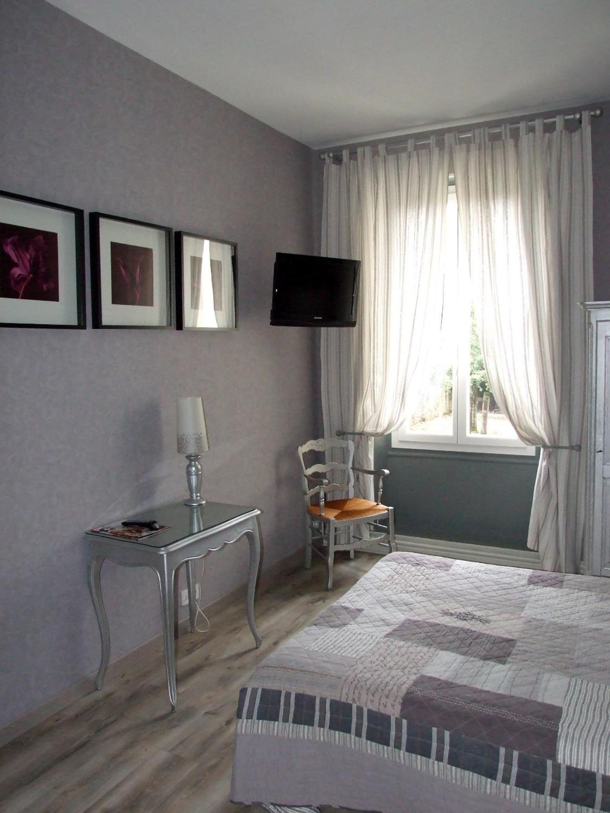 A bedroom with a bed, a desk, a chair, a television, and curtains.