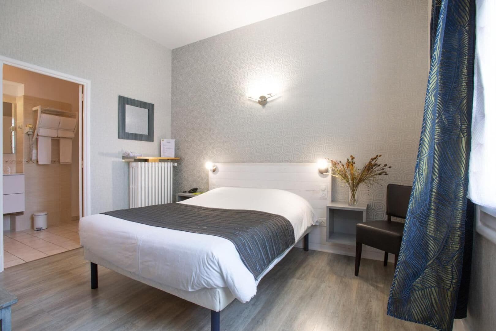 A hotel room with a bed, bedside table, lamp, and a view of the bathroom.