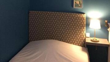 Un dormitorio con un cabecero estampado, una cama con ropa de cama blanca y una mesita de noche con lámpara.