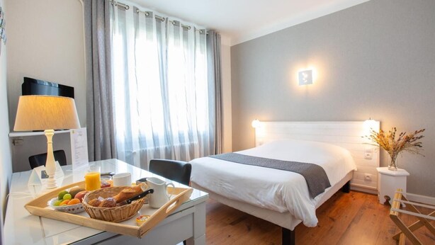 A hotel room with a bed, bedside table, lamp, and breakfast tray. - Hôtel l'Occitan (Gaillac)