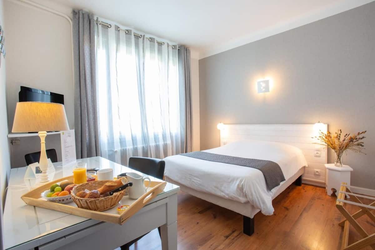 Une chambre d’hôtel équipée d’un lit, d’une table de chevet, d’une lampe et d’un plateau de petit-déjeuner.
