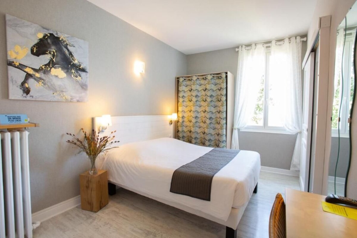 Una habitación de hotel con cama, mesita de noche, lámpara y un cuadro en la pared.