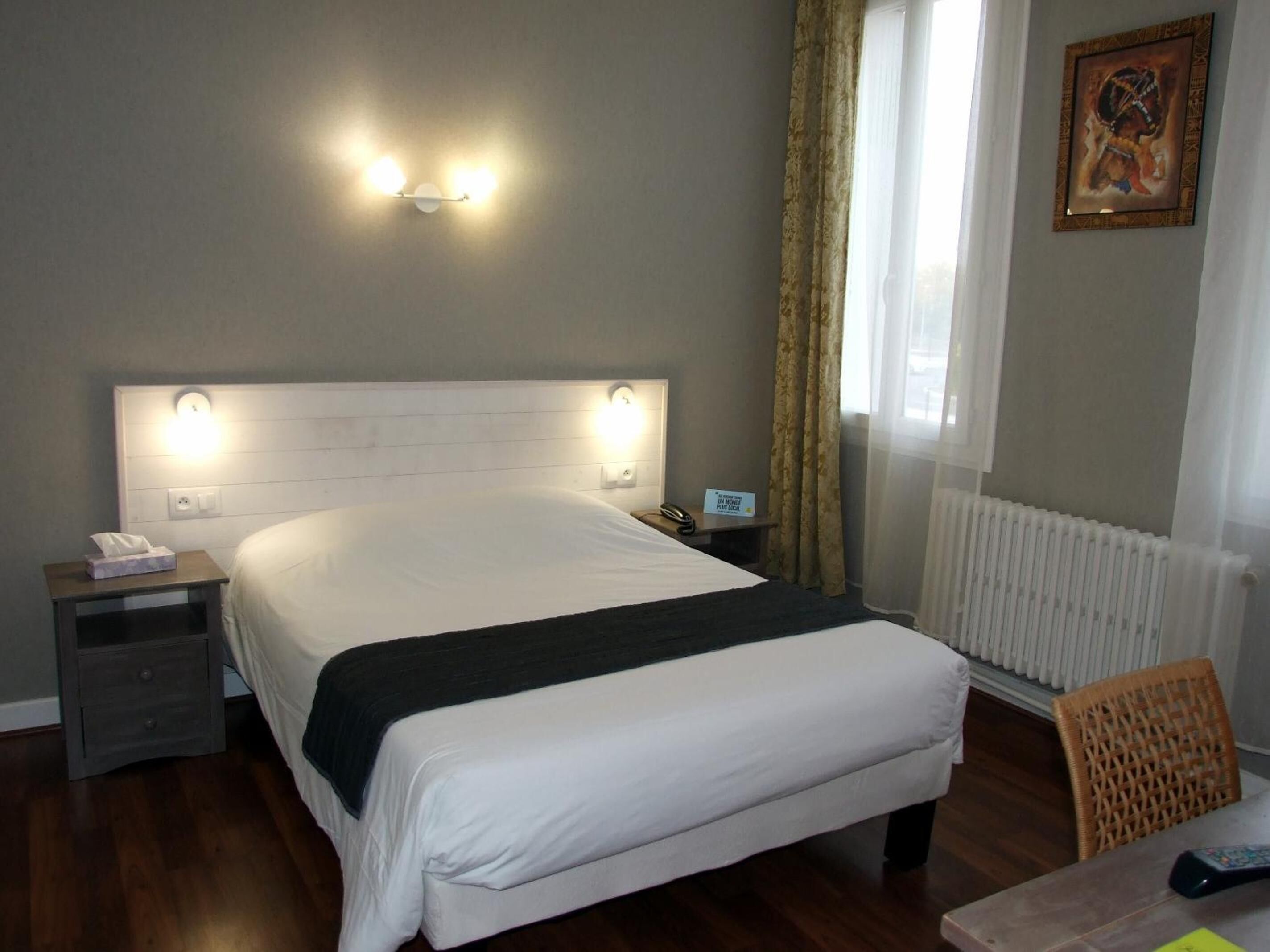 A hotel room with a large bed, bedside tables, a chair, and a painting on the wall.