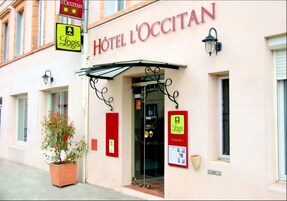 Exterior del Hotel L'Ocitan, con entrada despejada, una planta en maceta y señal de estacionamiento Logis.