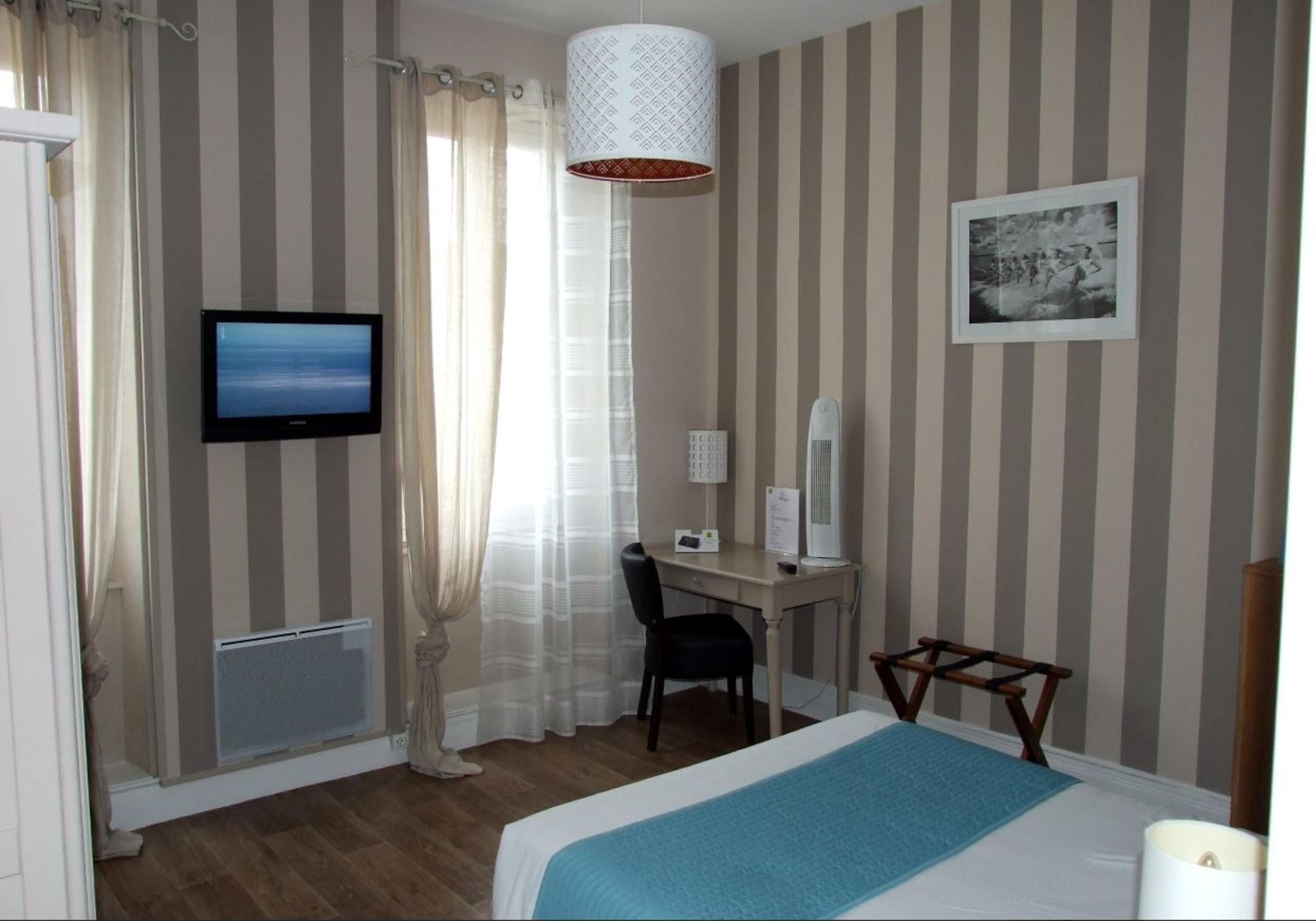 A hotel room with a bed, a desk with a computer, a television, a mirror, and a window with curtains.