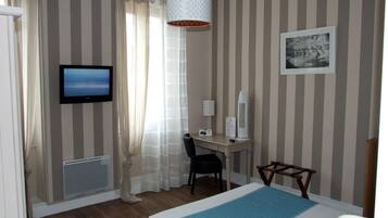 A hotel room with a bed, a desk with a computer, a television, a mirror, and a window with curtains.