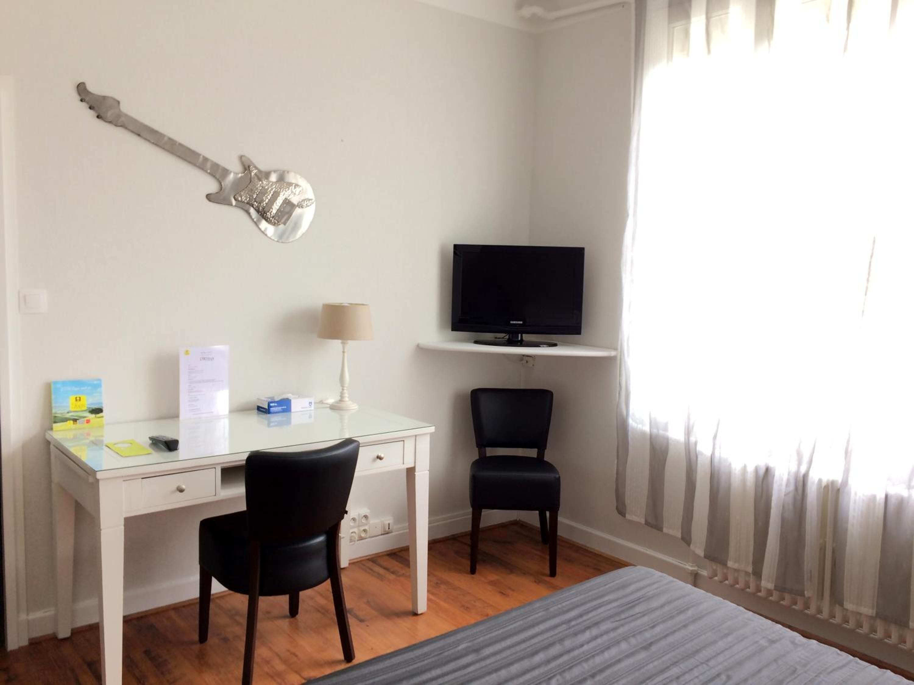 Een slaapkamer met een bed, een bureau met stoel, een televisie en een gitaar aan de muur.