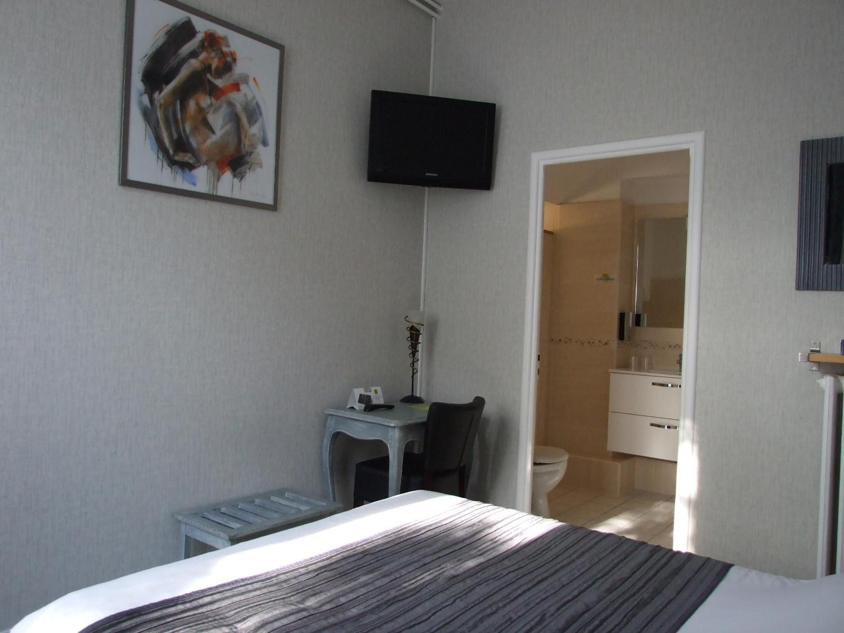 Hotelkamer met een bed, een bureau met stoel, een aan de muur bevestigde televisie en een badkamer door een open deur zichtbaar.