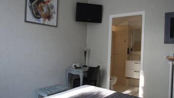 Hotelkamer met een bed, een bureau met stoel, een aan de muur bevestigde televisie en een badkamer door een open deur zichtbaar.