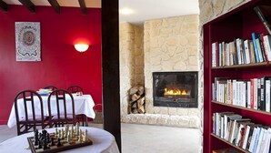 Una habitación acogedora con chimenea, un tablero de ajedrez, una estantería y una zona de comedor con sillas y mesa.