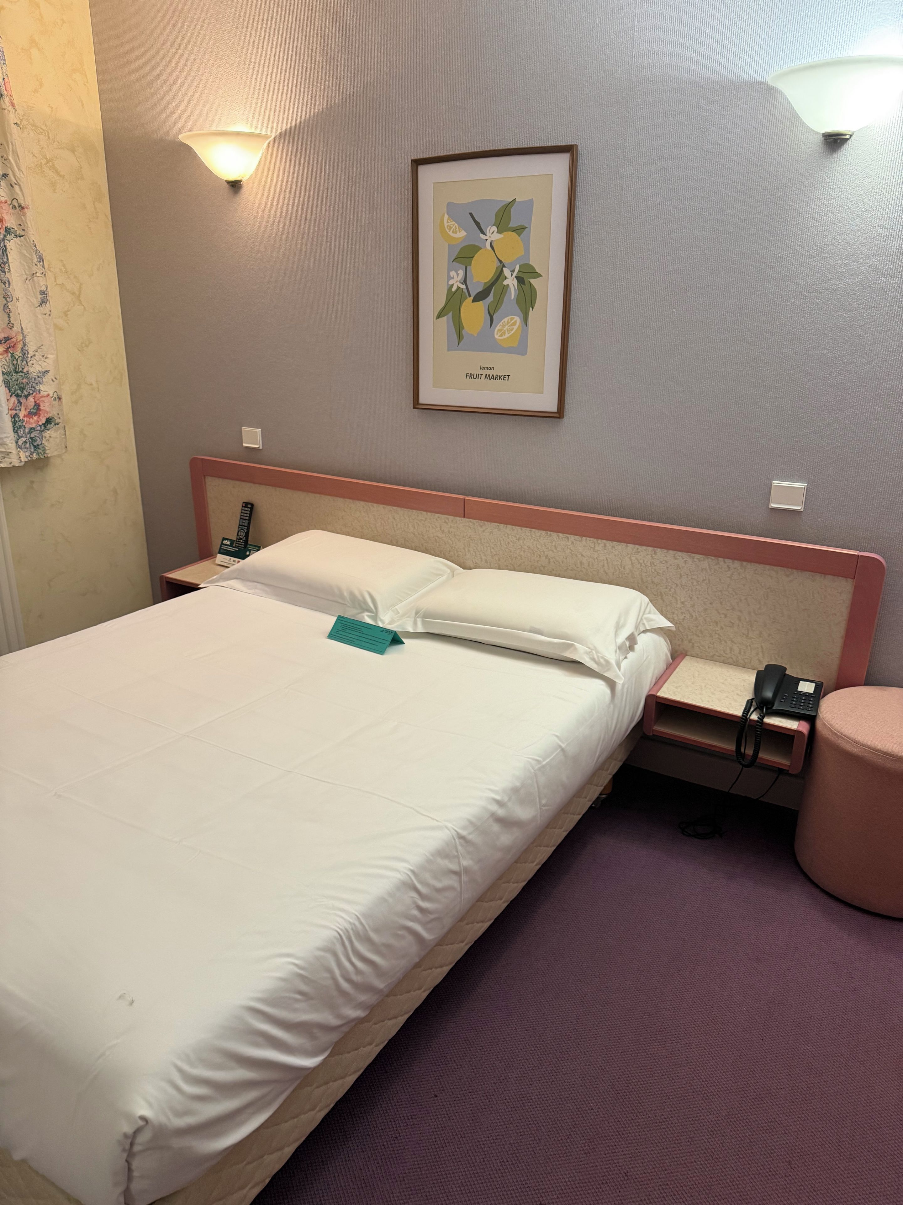 Habitación de hotel con cama, mesitas de noche, teléfono, lámpara y un cuadro en la pared.