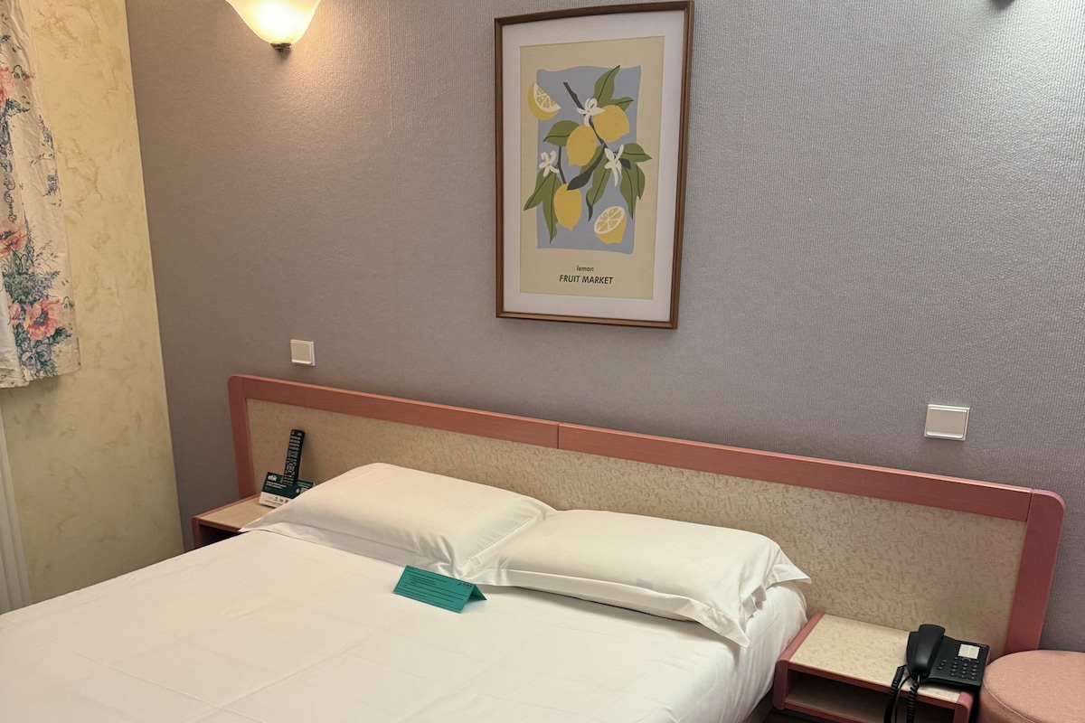 A hotel room with a bed, bedside tables, a phone, a lamp, and a framed picture on the wall.