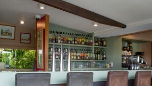 A bar area with four bar stools, a shelf of liquor bottles, and a counter with a coffee machine. - Hôtel du Lac (Lacapelle-Viescamp)