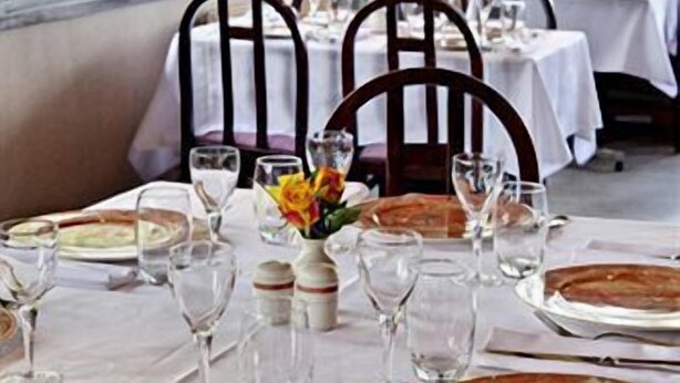 A dining area with tables set for a meal, chairs, and a view of greenery outside. - Hôtel du Lac (Lacapelle-Viescamp)