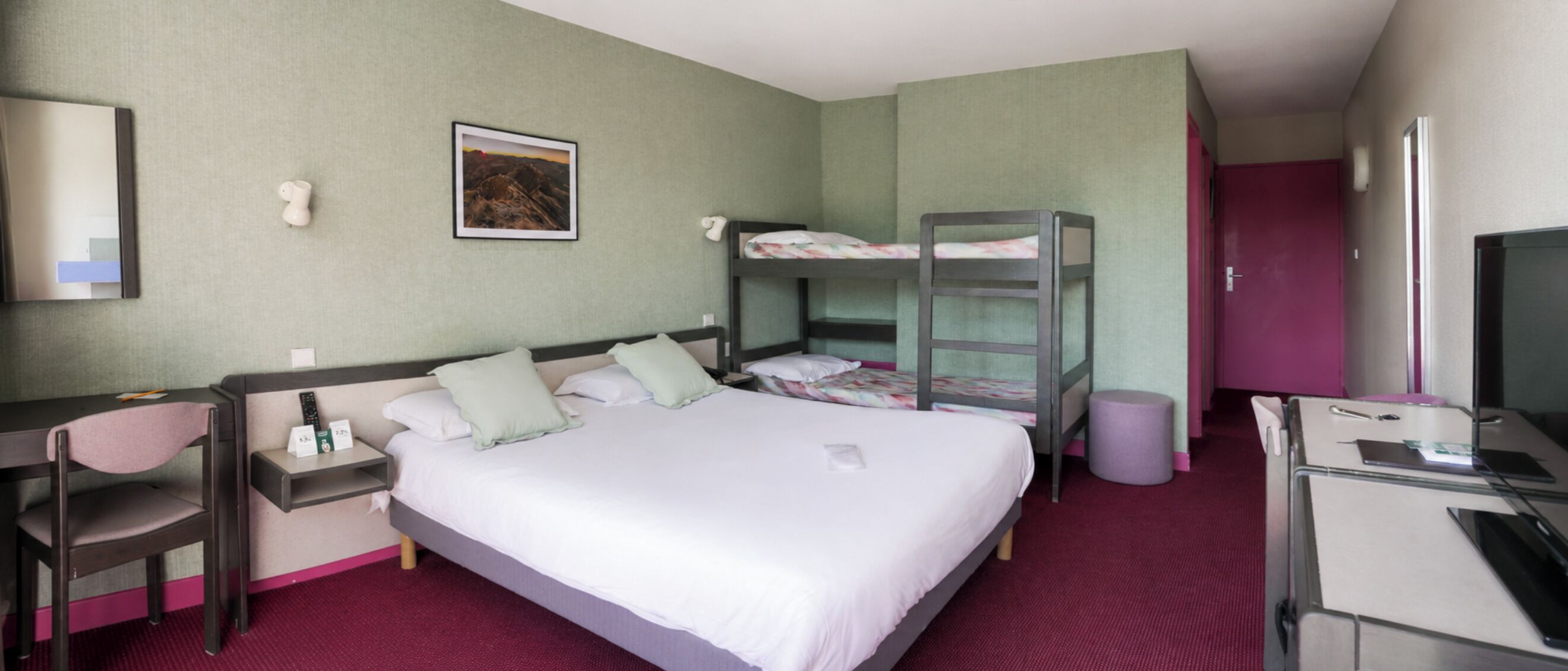 Una habitación de hotel con una cama, un escritorio, una silla, un televisor y una litera.